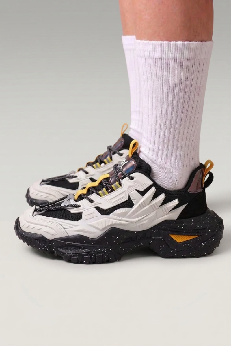 Baskets chunky 'Shinshiro' coloris blanc — lignes nervurées sur les flancs, semelle mouchetée, portées avec chaussettes blanches sur fond studio gris