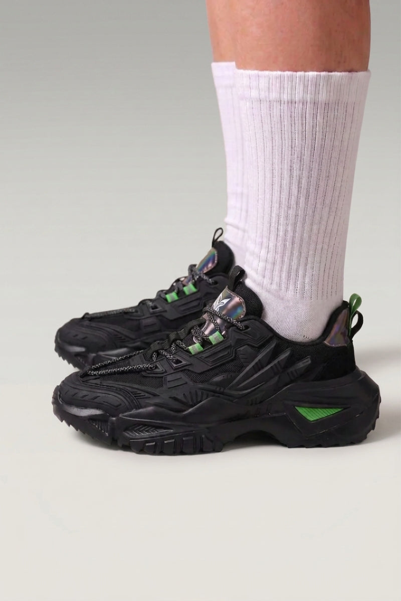 Baskets chunky 'Shinshiro' coloris noir — lignes nervurées sur les flancs, semelle mouchetée, portées avec chaussettes blanches sur fond studio gris