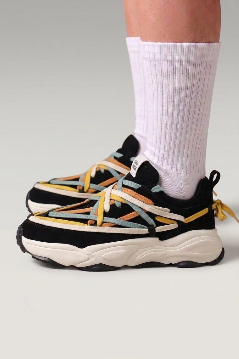 Baskets chunky 'Fujioka' coloris noir — double laçage multicolore, semelle épaisse crème, portées avec chaussettes blanches sur fond studio gris