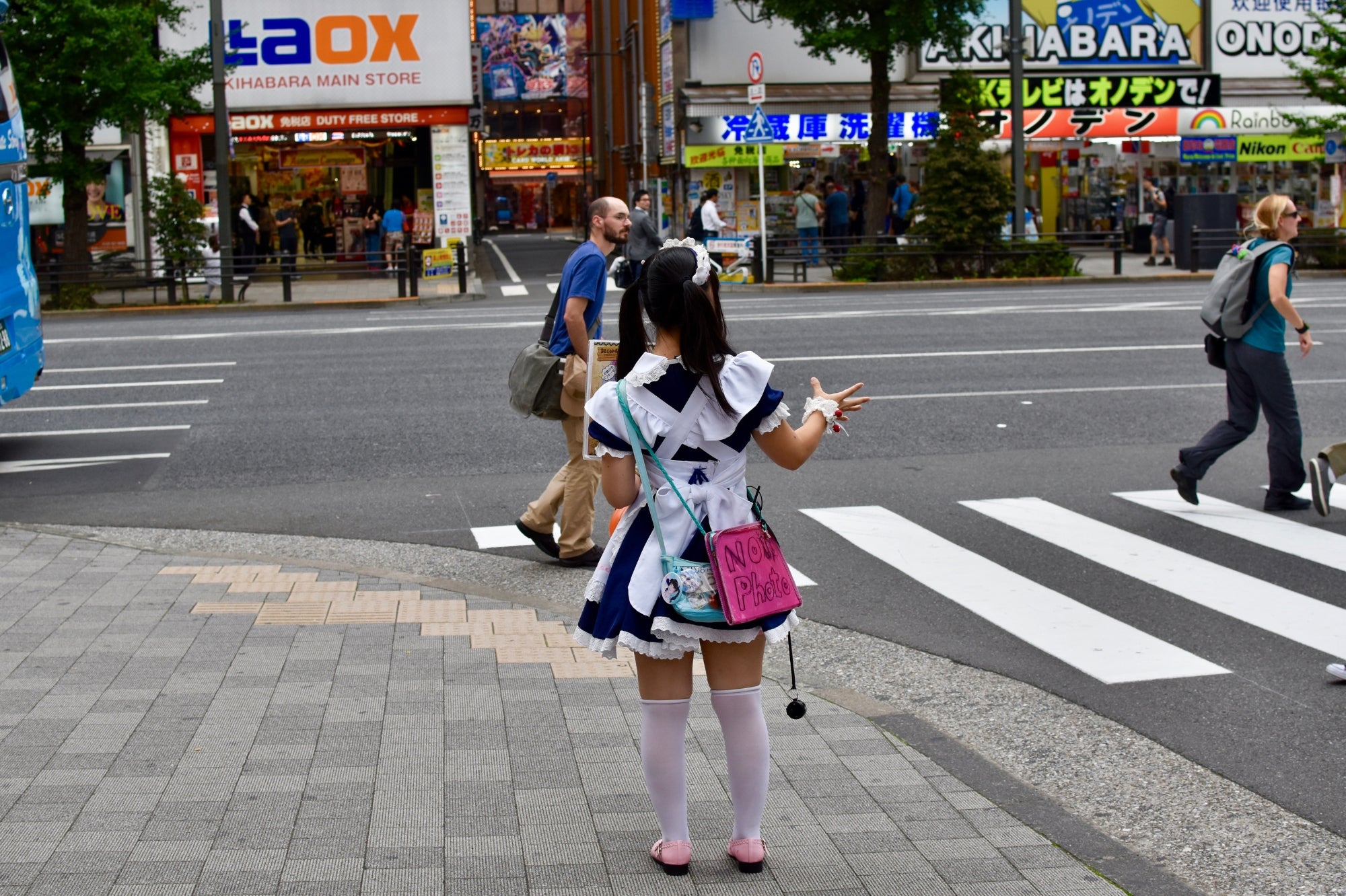 Jeune femme en uniforme de maid café à Akihabara, Tokyo, invitant les passants dans la rue, symbole de la culture otaku japonaise.