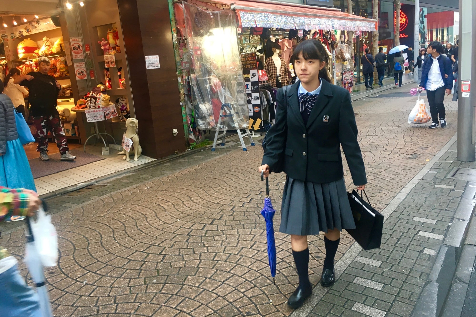 Lycéenne japonaise en uniforme marchant dans une rue commerçante de Harajuku, symbole du style et de la jeunesse à Tokyo.