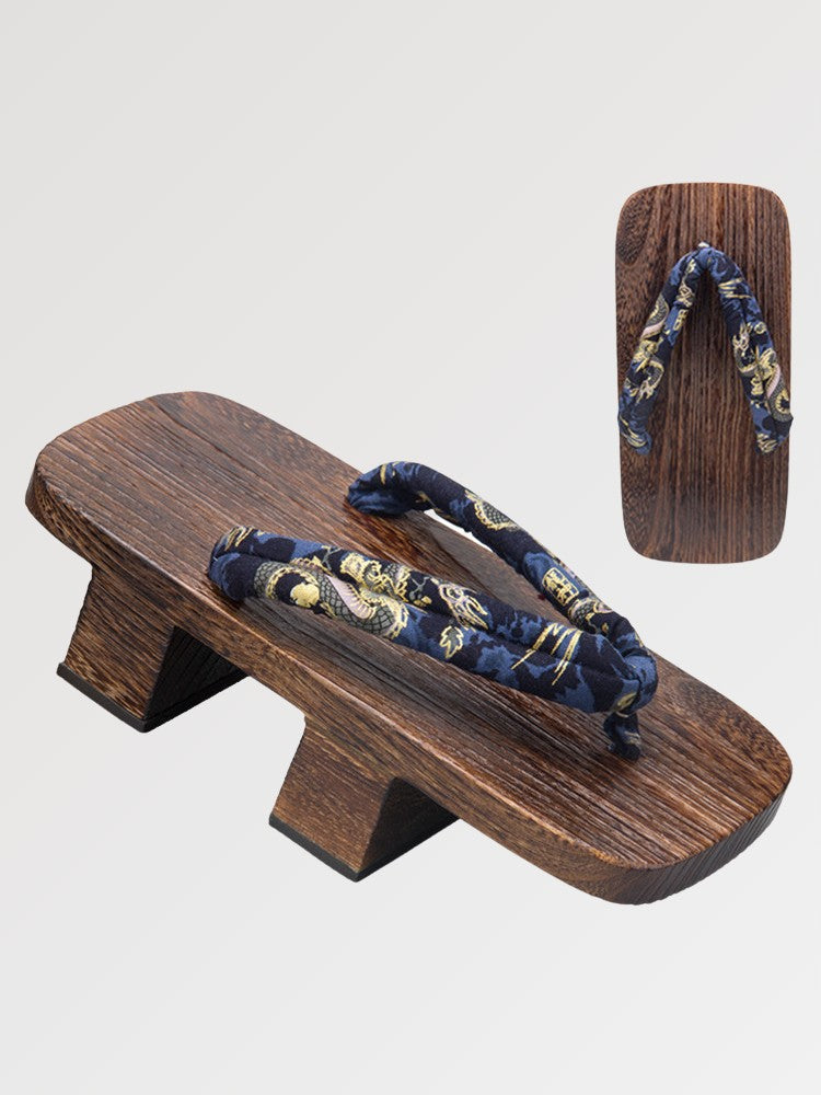 Paire de geta 'Inuyama' vue de trois quarts — socle en bois foncé à deux dents, lanière bleu nuit à motif floral doré, dessous visible