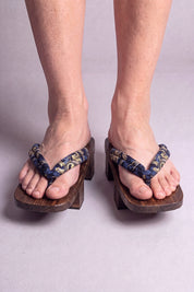 Geta japonaise 'Inuyama' portée pieds nus, vue de face — lanière bleu nuit à motif floral doré sur plateforme surélevée en bois foncé