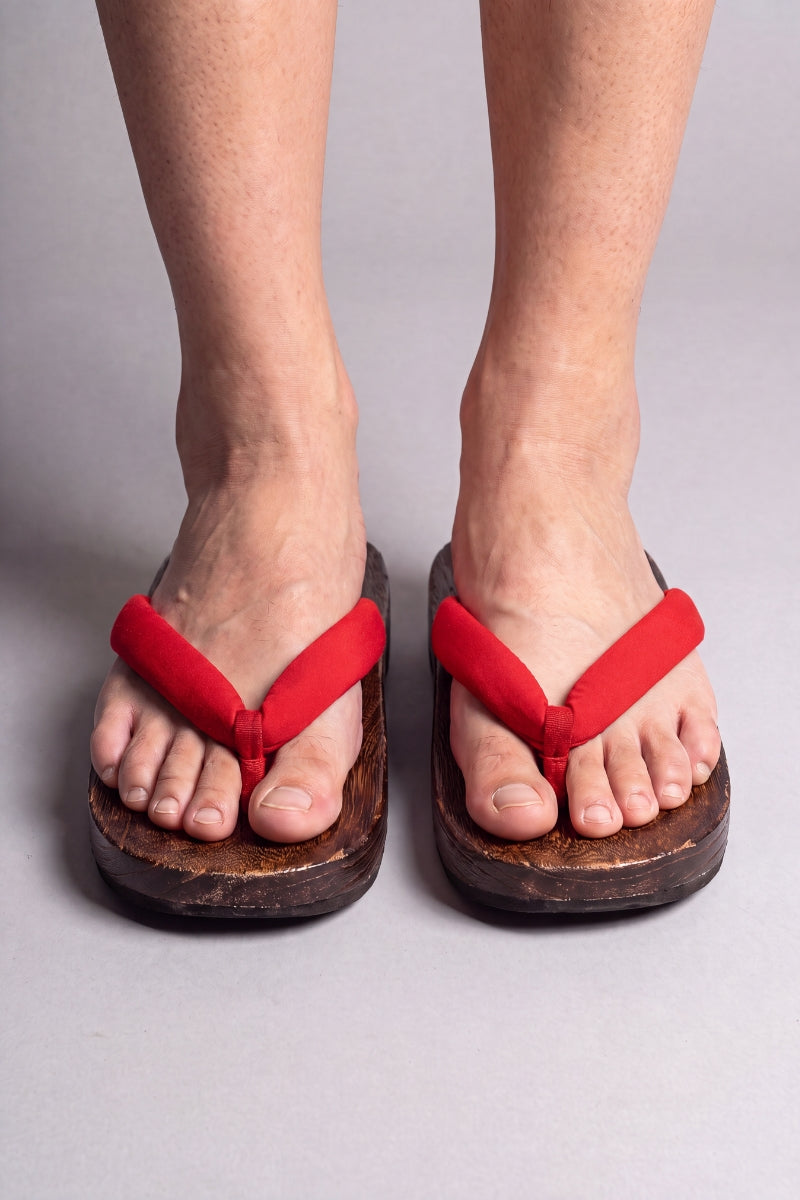 Tongs japonaises coloris rouge uni, portées pieds nus de face — semelle en bois massif brun et lanière rembourrée passant entre les orteils