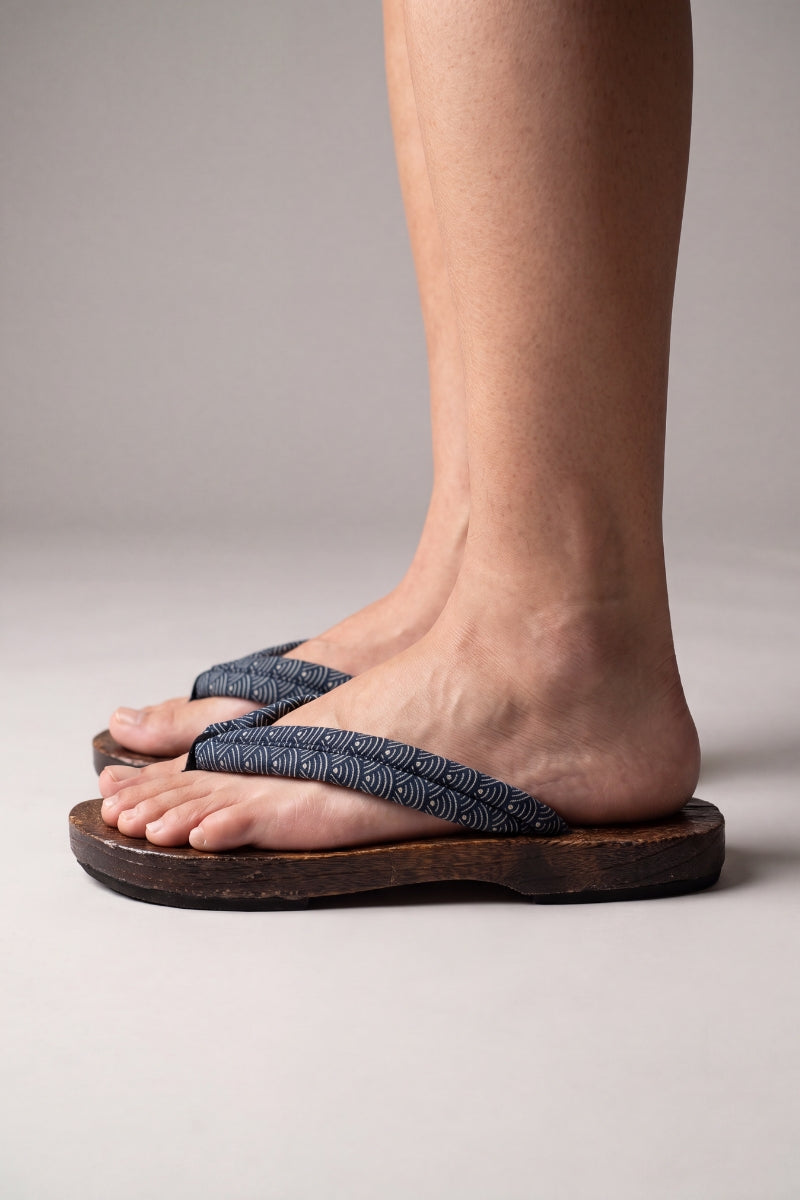 Tongs japonaises vues de profil, portées pieds nus — semelle en bois plate et galbée, lanière bleu-gris à motif de vagues
